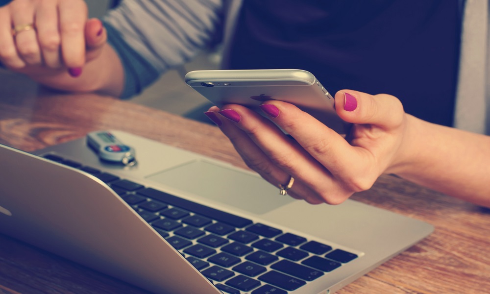 A person at a laptop holding a smartphone