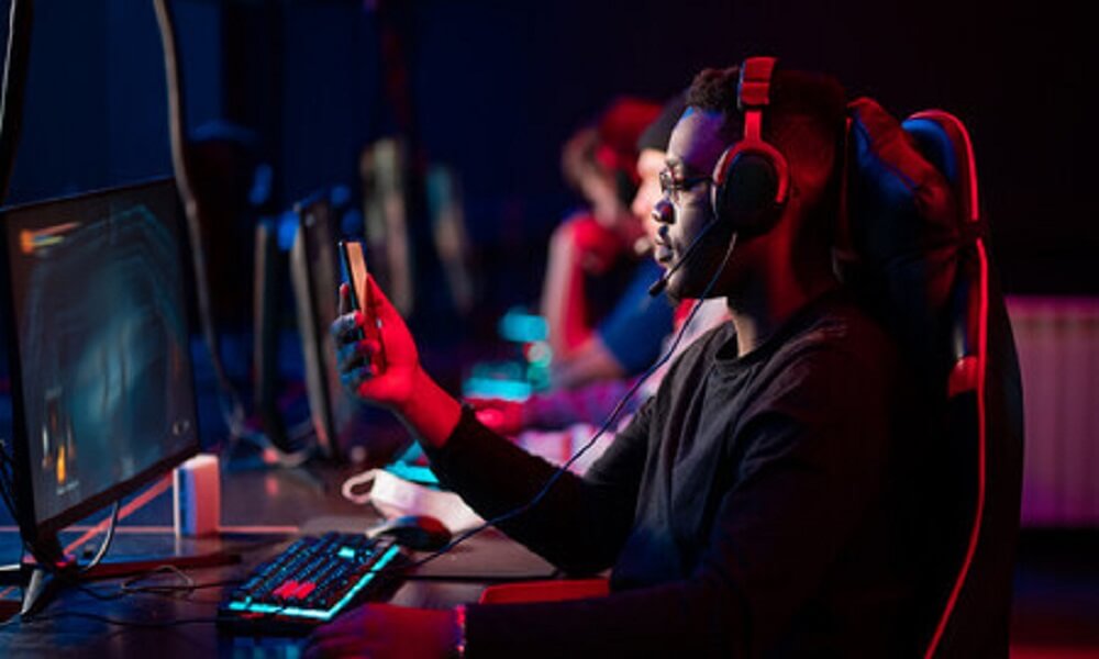 A man using his phone while playing video games on a computer.