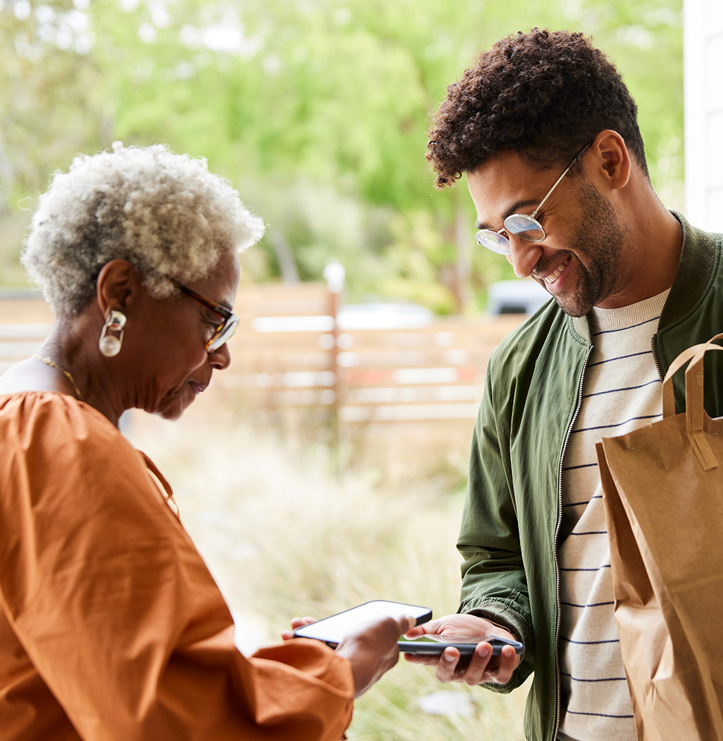 Woman interacting with delivery person, both smiling and looking at their phone